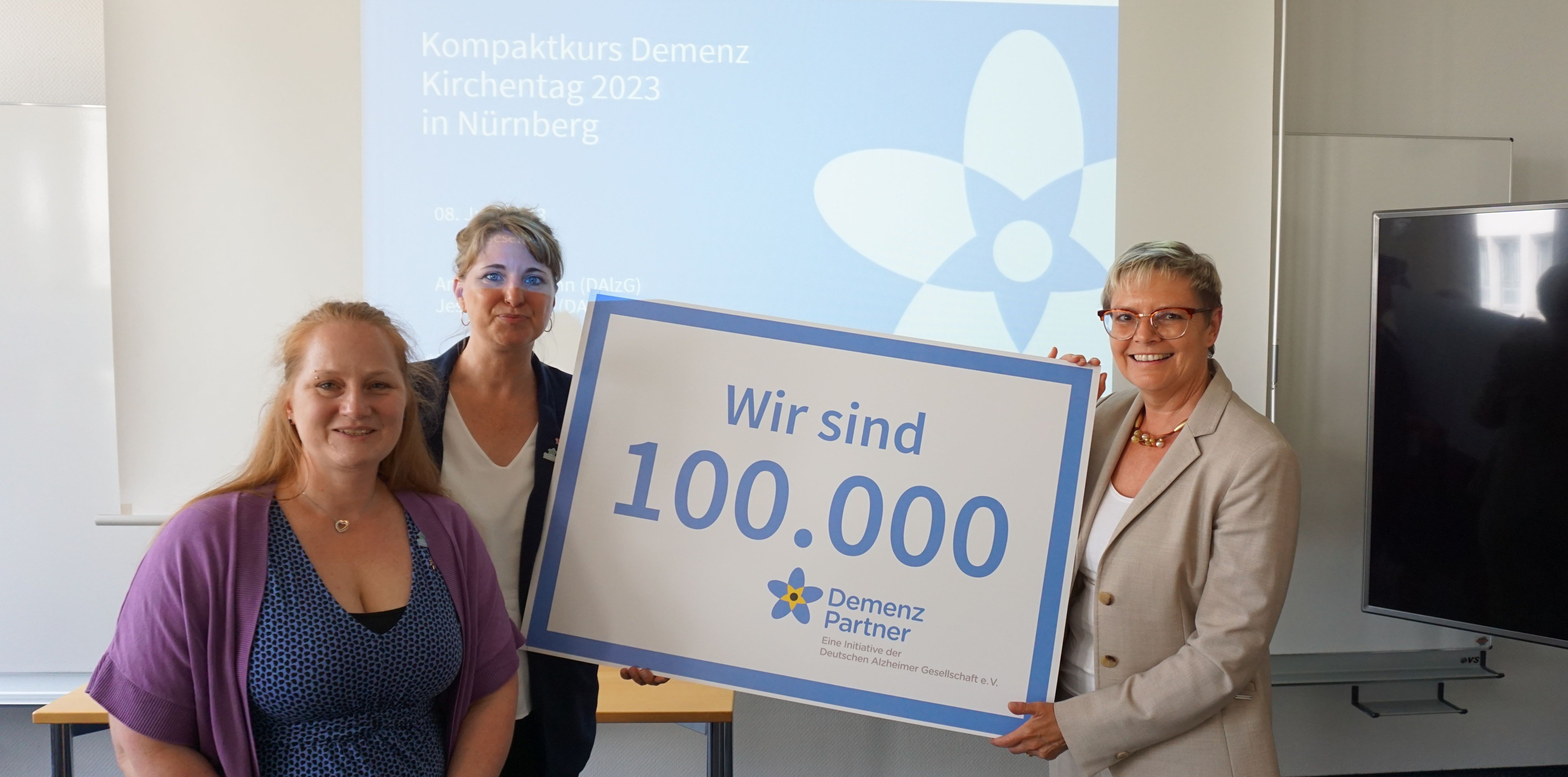 Jessica Dinter, Anna Gausmann und die Parlamentarische Staatssekretärin Sabine Dittmar (BMG) halten eine Tafel mit Aufschrift "Wir sind 100.000"